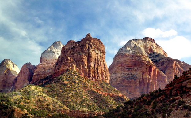 Eine malerische Aussicht auf den Zion-Nationalpark in Utah mit majestätischen Bergen, üppigen Bäumen, steinigem Gelände und einem Himmel mit weißen, flauschigen Wolken.