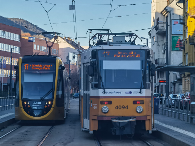 Zwei gelbe und weiße Straßenbahnen auf einer Stadtstraße mit hohen Gebäuden, Fahrzeuge auf der Straße, Geländer auf beiden Seiten und einem Hintergrund mit Gebäuden, Polen, Schildern, Bäumen, einem Hügel und dem Himmel.