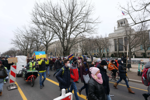 Eine große Gruppe von Menschen nimmt an einer Protestmarsch in Washington, D.C. am 21. Januar 2020 teil und geht eine Straße entlang mit Plakaten, Bannern und Fahrrädern, vor einem Gebäude mit Schildern, Bäumen und einem klaren blauen Himmel.