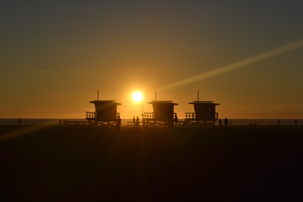 Sunset über Venice Beach, Kalifornien, mit Silhouetten von Lebensrettungstürmen und Menschen am Strand entlanglaufend.