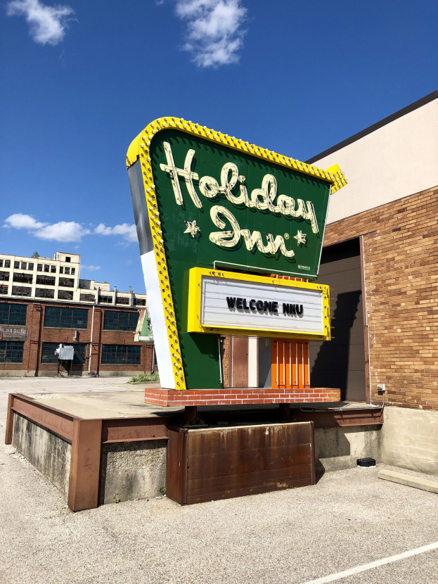 Holiday Inn-Schriftzug an einem Gebäude mit einem Textschild davor, bewölkter Himmel und sichtbaren Fenstern im Gebäude.