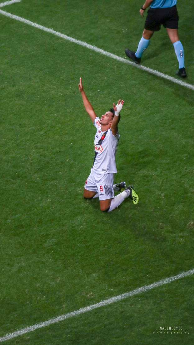 Fußballspieler kniet auf dem Boden und feiert mit ausgestreckten Armen, trägt Sportbekleidung und -schuhe.