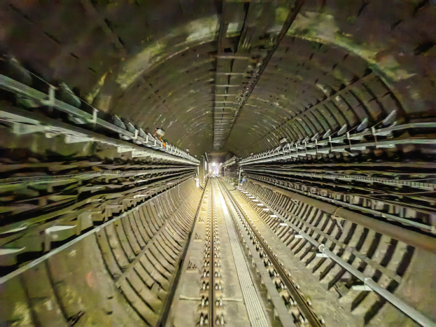 Ein Zug fährt durch einen schwach beleuchteten U-Bahn-Tunnel, mit ein paar Lichtern am Ende.