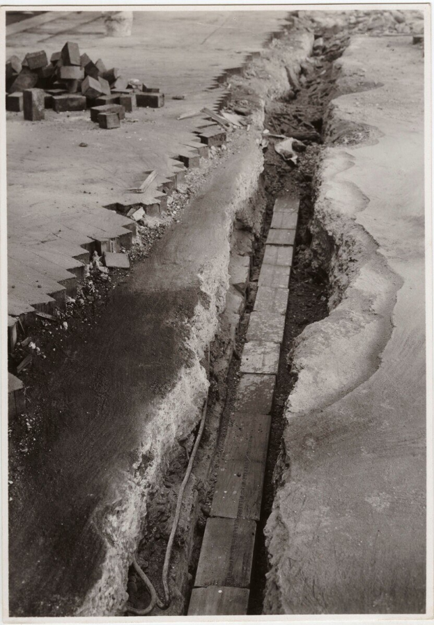 Schwarzes und weißes Foto einer Straße mit einem großen Riss und verstreuten Ziegeln auf der linken Seite.