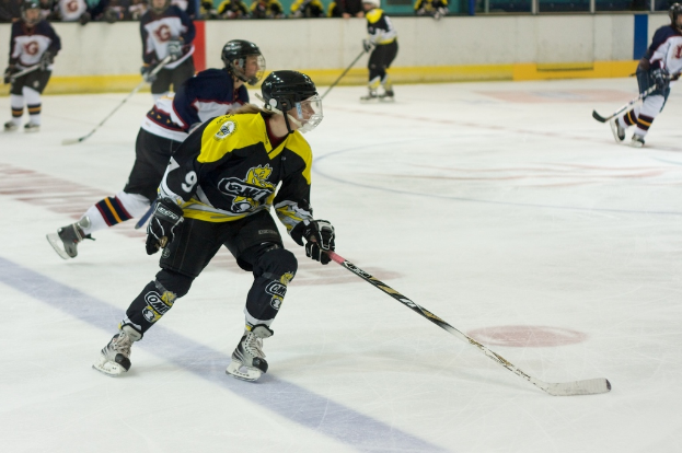 Menschen, die Eisstockschießen mit Eishockeyschlägern und Helmen spielen, mit anderen und einer Wand im Hintergrund.