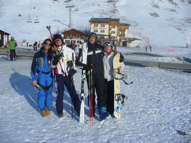 Vier Personen posieren mit Skaterausrüstung und Werkzeugen vor einer schneebedeckten Berglandschaft.