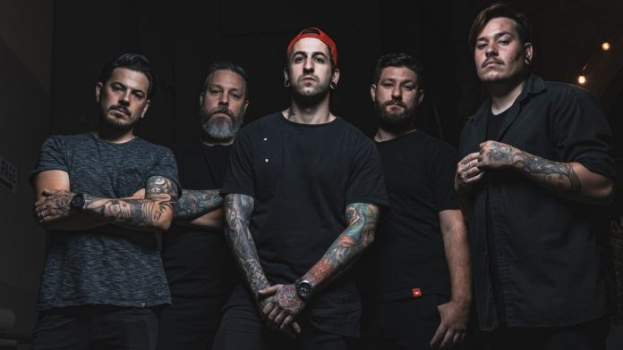 Eine Gruppe von Männern, die in einem dunklen Raum während eines Interviews stehen, von rechts beleuchtet, wahrscheinlich für Avenged Sevenfold.