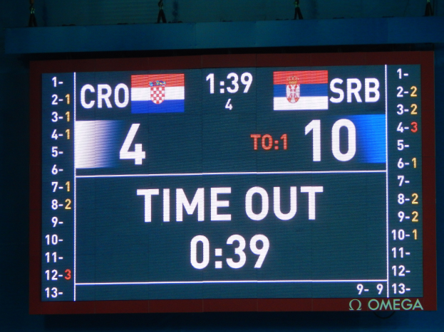 Ein großes elektronisches Scoreboard mit der Aufschrift "Kroatien vs. Serbien" mit Zahlen, Text und Flaggen, mit einigen Zuschauern oben auf dem Bild.