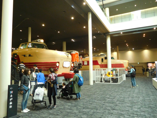 Eine Gruppe von Menschen vor einer Bahnausstellung in einem Museum, einige mit Taschen oder Kinderwagen und andere, die die Ausstellungen betrachten.