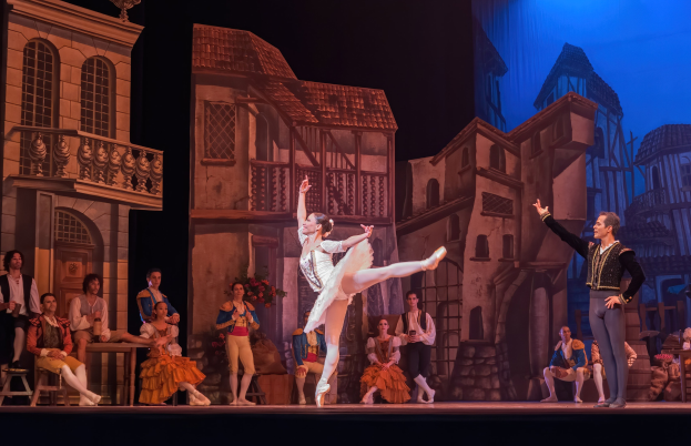 Zwei Tänzer performen auf einer Bühne im Royal Opera House in London, mit einem sitzenden und stehenden Publikum im Hintergrund.