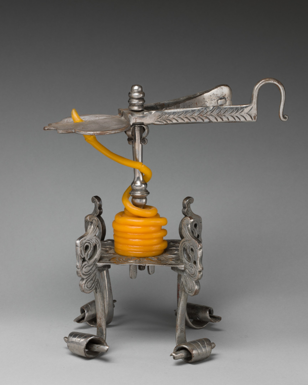 Metallischer Korkenzieher mit einer hellgelben Feder an seiner Oberseite, der einen zylindrischen Körper, einen Griff auf einer Seite und einen Ausguss auf der anderen Seite hat.