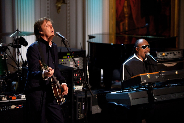 Paul McCartney und Stevie Wonder auf der Bühne der Grammys, wobei McCartney Gitarre spielt und singt und Wonder eine Brille trägt, während er am Piano spielt.