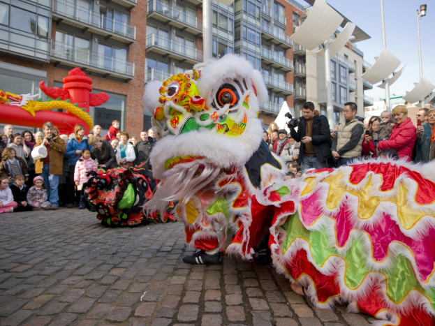 Ein lebendiges chinesisches Neujahrsfest in Amsterdam mit einer Löwen-Tanzvorstellung vor einem Publikum mit Kameras und einem klaren blauen Himmel im Hintergrund.