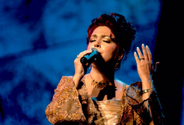 Frau in goldnem Kleid singend ins Mikrofon auf der ESC-Bühne mit blau-schwarzem Hintergrund.