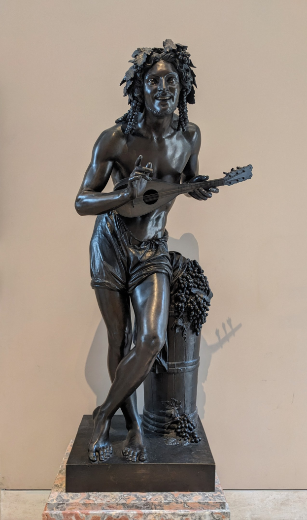 Bronzestatuette eines Mannes mit einer Gitarre spielend, mit einer Wand und einem Boden im Hintergrund.