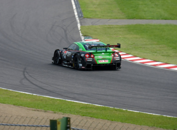 Ein weißer Toyota Supra GT3-Rennwagen mit Sponsorentext und Nummern auf einer Rennstrecke, mit einer Begrenzung und Gras im Hintergrund.