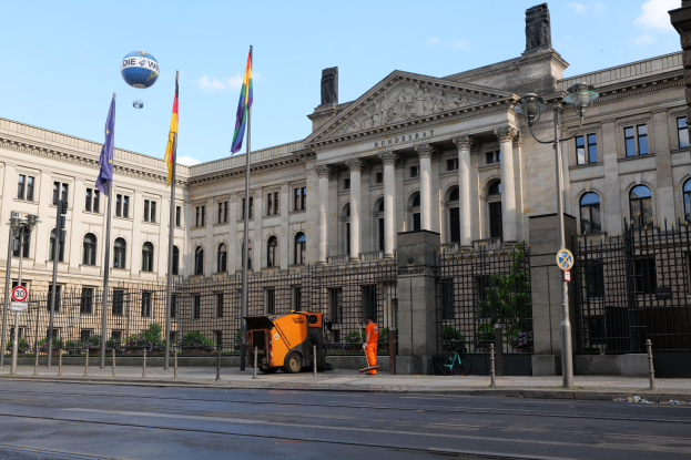 Großes modernes Gebäude mit vielen Fenstern, als Bundestag in Berlin, Deutschland identifiziert, umgeben von Straßeninfrastruktur, Fahrzeugen, Fußgängern und Bäumen unter einem bewölkten Himmel.