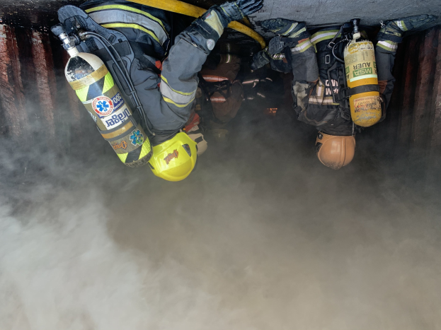 Feuerwehrleute in Schutzausrästen arbeiten daran, ein Tunnelbrand zu löschen, bei dem Rauch aus der Tiefe aufsteigt.