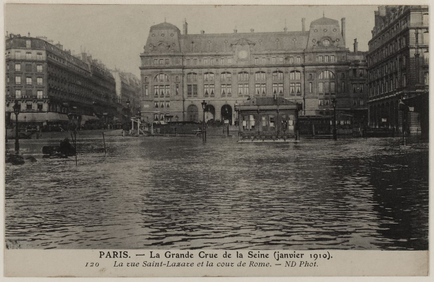 Schwarz-weiß-Foto einer überfluteten Straße in Paris mit Gebäuden, Straßenlaternen, Straßenlaternen, Kraftfahrzeugen und einem Himmel im Hintergrund, mit Text unten.