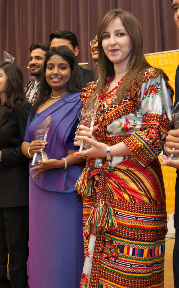 Eine Gruppe von Menschen auf einer Bühne mit einer Frau in der Mitte, die eine Trophäe hält, hinter einem Vorhang mit einer Tafel, auf der "Bravo Segenspreise-Gewinner" steht.