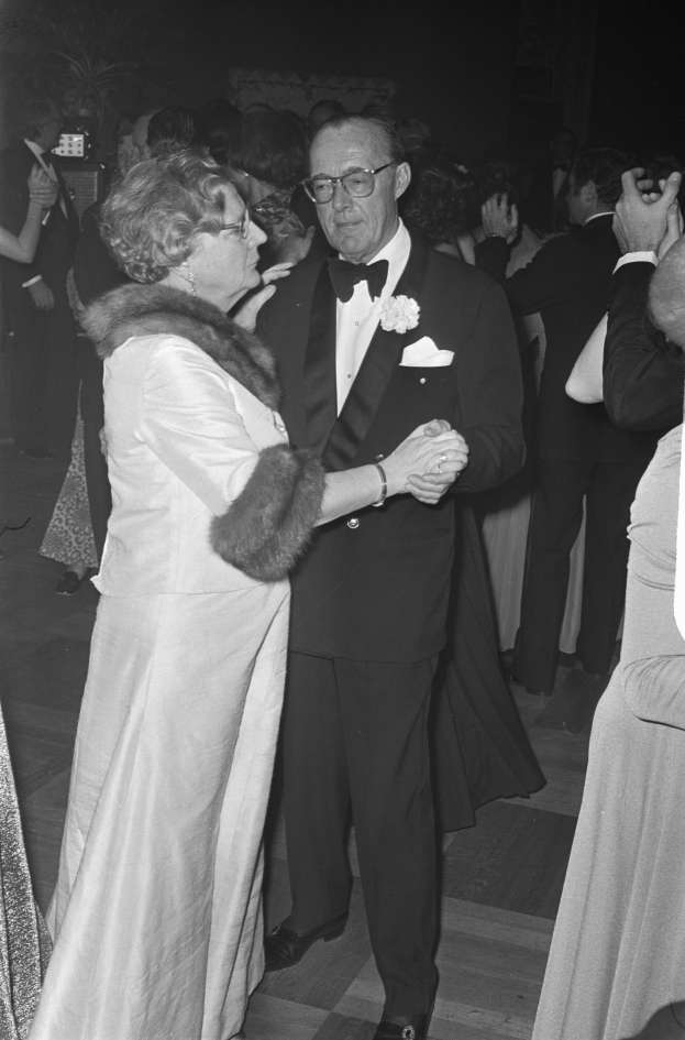 Formal gekleideter Mann und Frau tanzen zusammen auf einer Party, umgeben von anderen und einigen mit Kameras im Hintergrund.