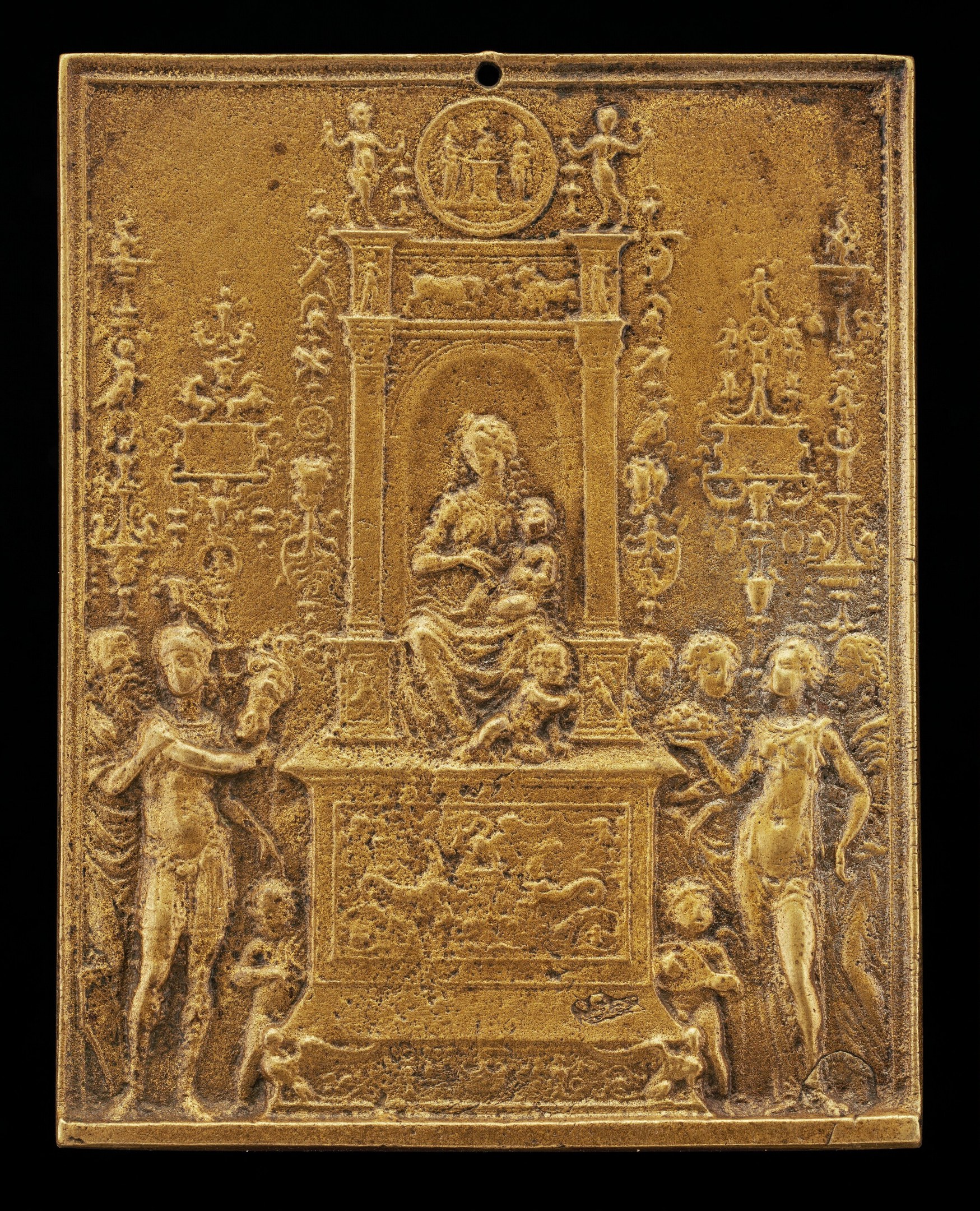 Goldene Plakette mit detailreicher Skulptur einer Frau in einem wallenden Kleid und eines Mannes in Anzug und Krawatte auf schwarzem Hintergrund, umrahmt von einem goldenen Rahmen.