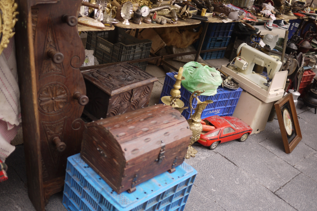 Ein Flohmarktstand mit Holzboxen, einem Spielzeugauto, einer Nähmaschine, einem Foto Rahmen, einer Uhr und anderen diversen Gegenständen auf Tischen.