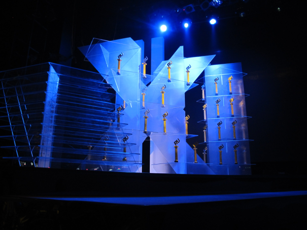 Eine Bühne für eine Preisverleihung mit dunklem Hintergrund, beleuchtet von ein paar Lichtern und mit ein paar Gegenständen, die mit dem Event in Verbindung stehen.