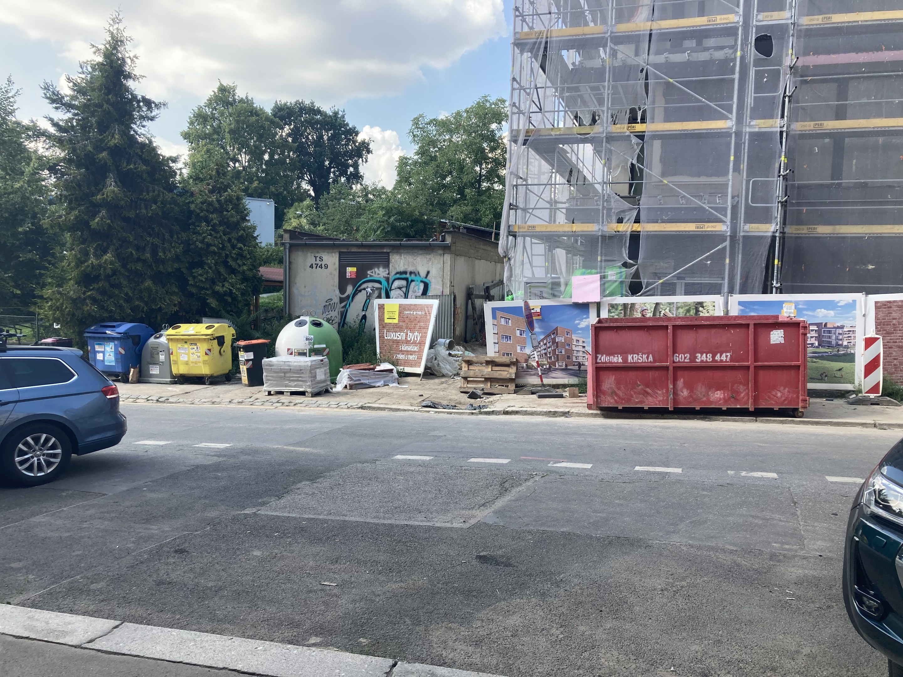 Zwei Autos neben einem Gebäude in Bau neben einem Gebäude mit verstreuten Trümmern, Bäumen und einem bewölkten Himmel im Hintergrund.