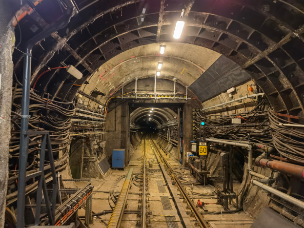 Ein Tunnel mit einer Bahnschiene, beleuchtet von Lampen an der Decke, mit Pfählen und Drähten auf beiden Seiten und einem blauen Objekt in der Mitte, Teil der Londoner U-Bahn.