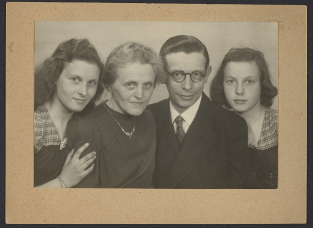 Schwarzes und weißes Foto einer Familie, die zusammen posiert, mit einem Mann im Anzug und Krawatte flankiert von zwei strahlenden Frauen.