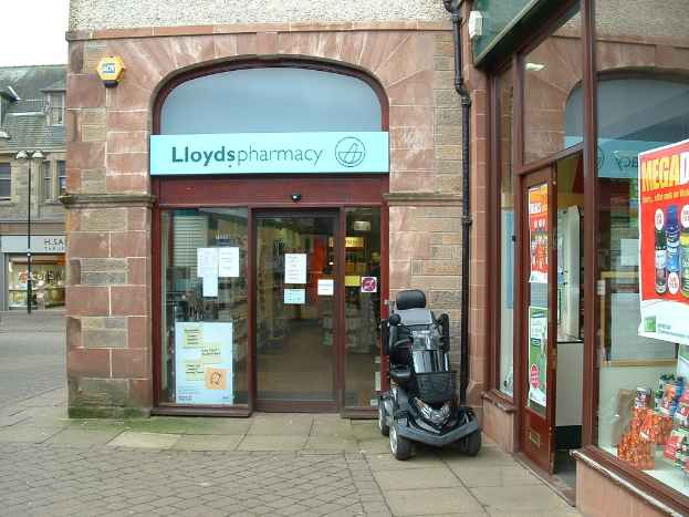 Ein Apothekenladen mit einem vor ihm geparkten Fahrzeug und einem Gebäude in der linken Ecke.