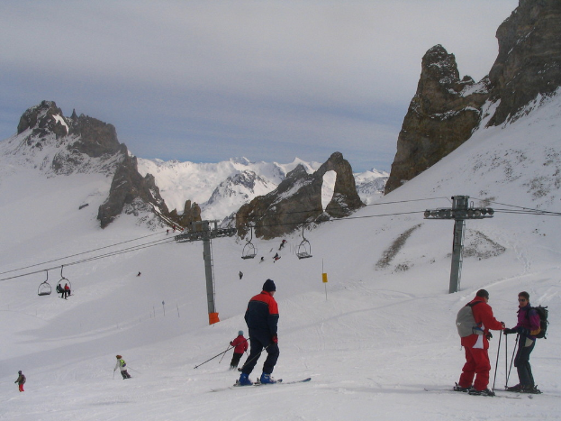 Menschen in Pullovern fahren auf dem Eis Ski mit einer Seilbahn, Bergen und einem bewölkten Himmel im Hintergrund.