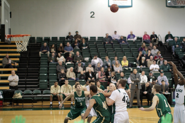 Ein Basketballfeld mit aktiv spielenden Spielern und Zuschauern im Hintergrund.