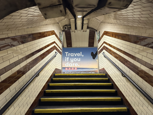 Eine Treppe in einer U-Bahn-Station mit Geländern auf beiden Seiten, die zu einem Schild führt, das 'Reise, wenn du wagst.' lautet.