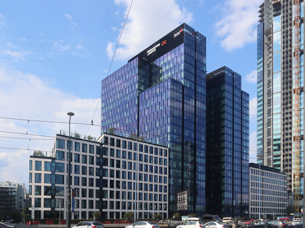Zentrale der Deutschen Bank in Frankfurt, Deutschland, ein großes Gebäude mit vielen Fenstern, umgeben von Straßeninfrastruktur, Fahrzeugen, Grünflächen und einem bewölkten Himmel.