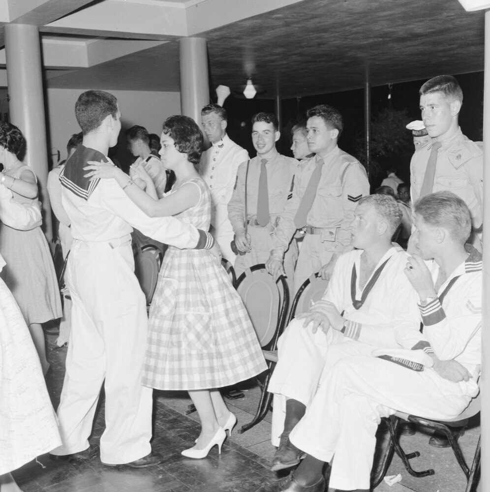 Eine Gruppe von Männern in traditioneller amerikanischer Ureinwohner-Kleidung führt einen Kriegstanz auf einem buntfarbenen Papier mit sichtbarem Text aus.