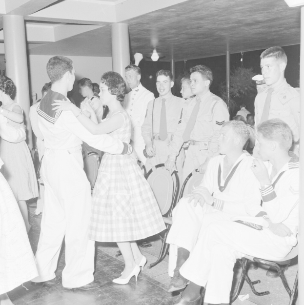 Eine Gruppe von Männern in traditioneller amerikanischer Ureinwohner-Kleidung führt einen Kriegstanz auf einem buntfarbenen Papier mit sichtbarem Text aus.