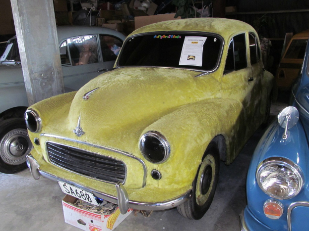 Mehrere Oldtimer stehen vor einer Wand mit verschiedenen Zubehörteilen, links ist eine Säule zu sehen.