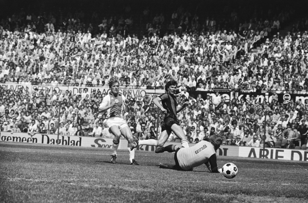 Schwarzes Foto von Männern, die auf einem Feld Fußball spielen, mit Zuschauern im Hintergrund und einem Banner "Bundesliga 1978-79 Ajax 1-1 Hannover 96".