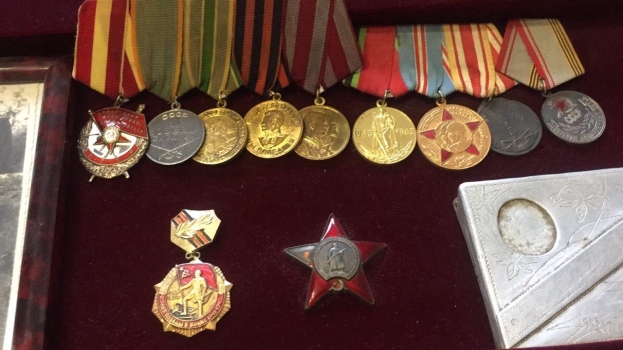 Eine hölzerne Kiste mit verschiedenen Medaillen, darunter ein roter Stern, ordentlich mit einem Objekt auf der rechten Seite.