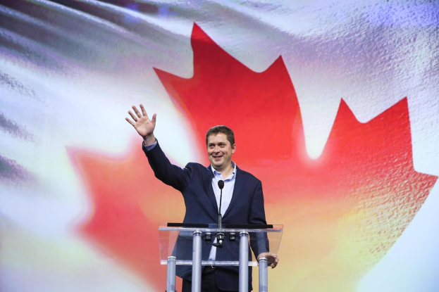 Der kanadische Premierminister Alex Salmond steht an einem Podium mit Mikrofonen, lächelt, vor einer kanadischen Flagge mit einem Bildschirm im Hintergrund.