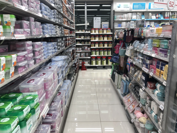 Ein unordentlicher chinesischer Supermarktgang mit Regalen voller Kisten, Flaschen, Tüten und anderen Artikeln, mit Texttafeln, Beleuchtung und einem sichtbaren Feuerlöscher auf dem Boden.