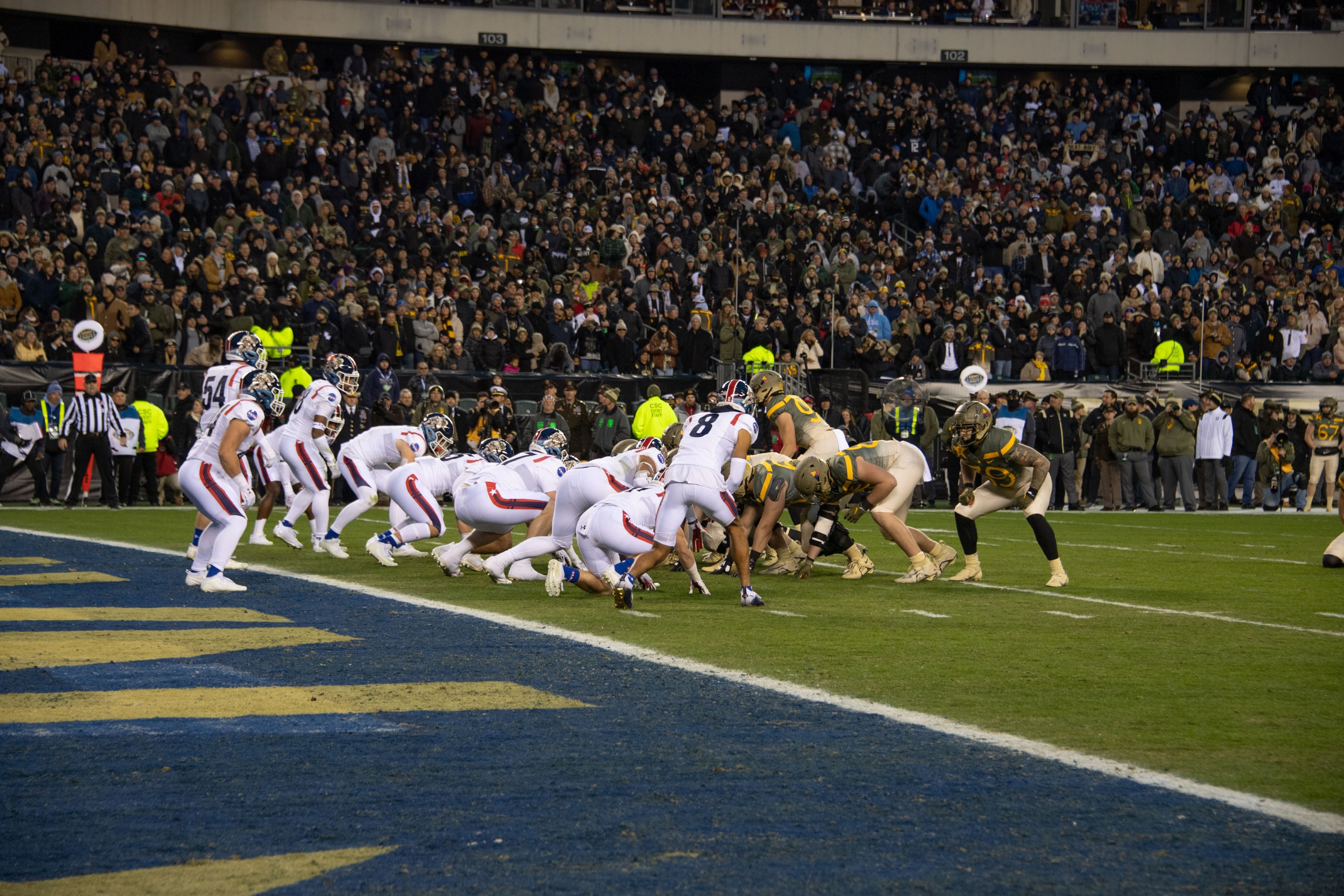 Fußballspieler in Sportkleidung und Helmen auf dem Boden während eines Spiels in einem Stadion mit Zuschauern und Anzeigetafeln im Hintergrund.