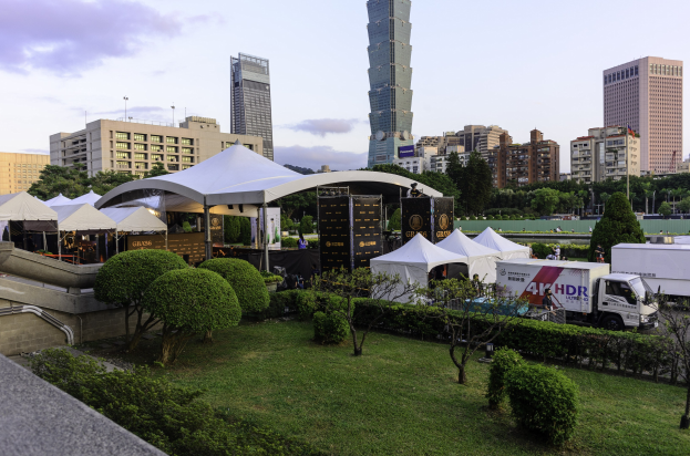 Gruppe von Zelten in einem Park mit Grünfläche, Menschen, Fahrzeugen, Gebäuden und einem klaren Himmel, wahrscheinlich beim Hong Kong International Film Festival.