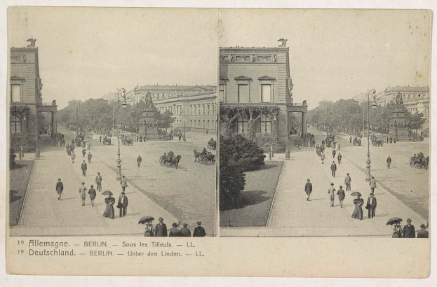 Ein altes Schwarz-Weiß-Foto von Menschen, die eine Straße in Berlin, Deutschland, entlanggehen, mit Gebäuden, Bäumen, Pfählen, Laternen, Statuen und Menschen mit Schirmen im Vordergrund und Text am unteren Bildrand.