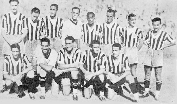 Ein Schwarz-Weiß-Foto einer Fußballmannschaft, bei dem einige Spieler stehen und andere auf dem Boden sitzen, mit Text unten.