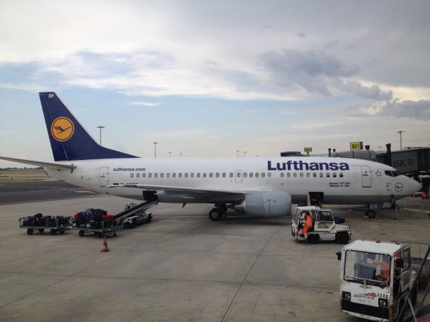 Lufthansa Airbus A320-200 am Frankfurt Airport mit Bodenfahrzeugen, Wagen, Verkehrskegeln, Schildern und einem bew├Âlktem Himmel im Hintergrund.