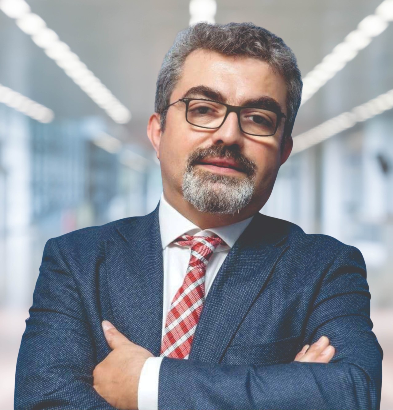 Ein Mann in Anzug und Krawatte mit verschränkten Armen und Brille, der vor einem unscharfen Hintergrund steht, als der neu ernannte Marketingchef identifiziert.