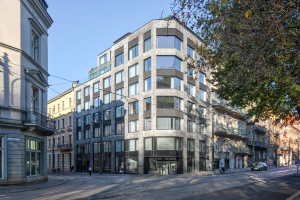 Großes Bürogebäude mit mehreren Fenstern, umgeben von Straßeninfrastruktur, Fahrzeugen, Fußgängern, Bäumen und einem bewölkten Himmel als neue Firmenzentrale.